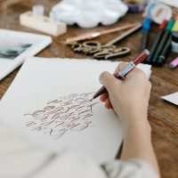 Personne en train de dessiner des lettres sur une table entourée de stylos de couleurs vives.